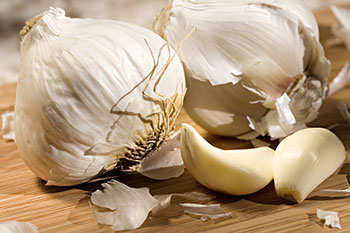 two heads of fresh garlic flanked by two garlic cloves