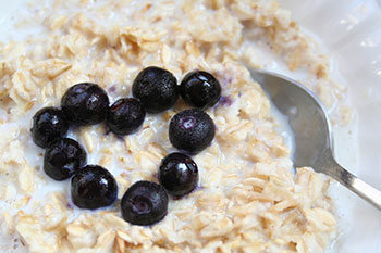 a closeup of a bowl of cooked oatmeal topped with blueberries in a heart shape