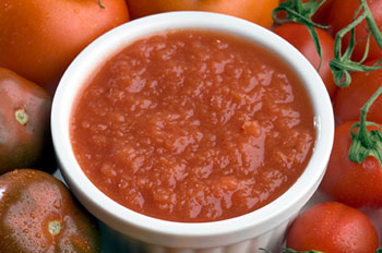 A bowl of tomato sauce surrounded by ripe red tomatoes