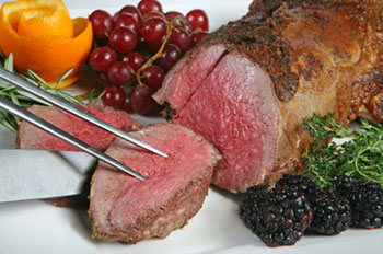 a beef tenderloin being sliced with a knife and fork, with grapes and blackberries for garnish
