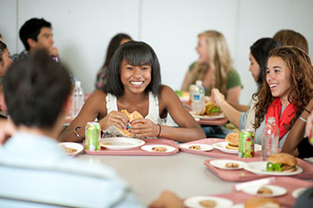 a group of adolescents having lunch together around a table in a school lunchroom