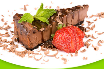 a slice of chocolate cheesecake garnished with curls of chocolate and a sliced strawberry