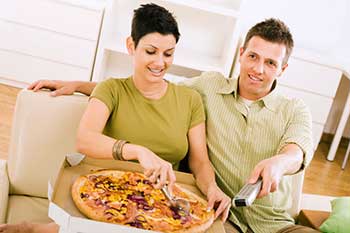 A young man and woman eating pizza while watching television