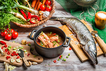 Ingredients for a fish soup, including a whole fish, tomatoes, leeks, carrots, garlic, and other vegetables