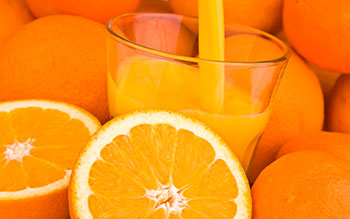 a glass of orange juice surrounded by sliced and whole oranges