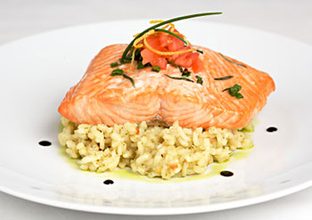roasted salmon placed on top of a lemon basil risotto, with sauce dotted around the edge of the plate