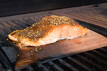 a filet of salmon roasting on a cedar plank over a fire in a wood grill