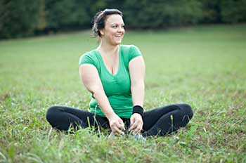a person in exercise clothing sitting cross-legged in the grass, smiling