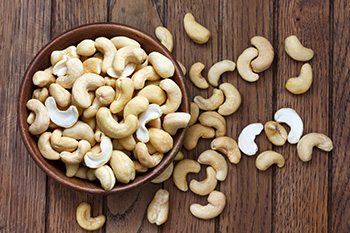 a glass bowl of cashew nuts with nuts scattered on the table in the background