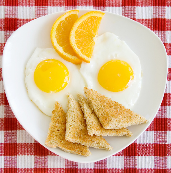 A plate of fried eggs and wheat toast garnished with orange slices
