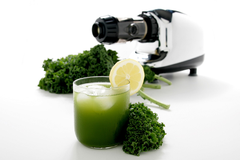 A glass of kale juice with fresh kale and a juicer in the background