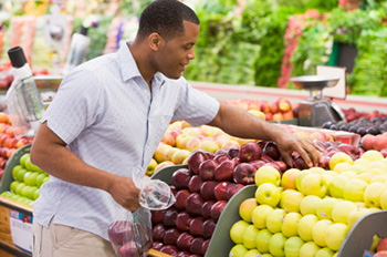 an African-American man choosing apples in the produce section of a grocery store