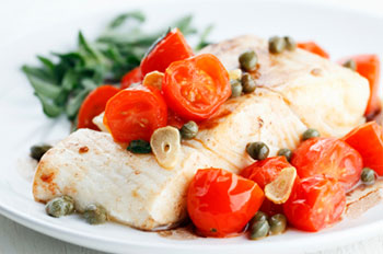 a filet of seared halibut topped with a sauce made of roasted cherry tomatoes, sliced garlic, and capers