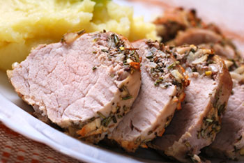 a sliced, roasted pork tenderloin on a white plate with mashed potatoes in the background