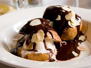 two vanilla ice cream profiteroles topped with chocolate sauce and slivered almonds