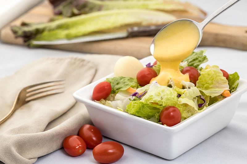 salad dressing is drizzled onto a fresh salad using a spoon
