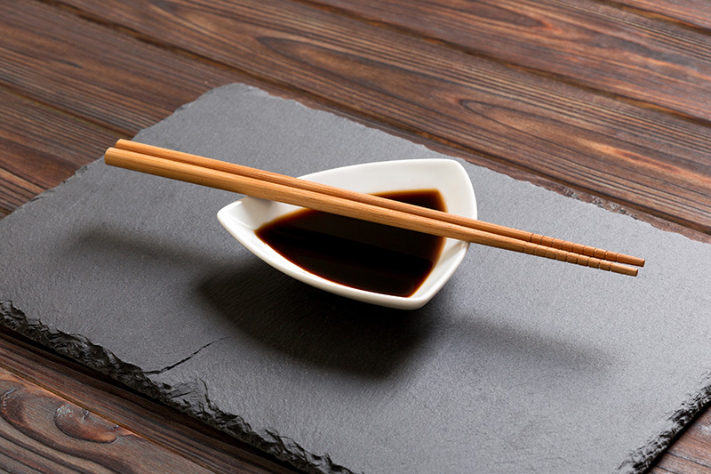 a small triangular dish of soy sauce with chopstick balanced across the top of the bowl