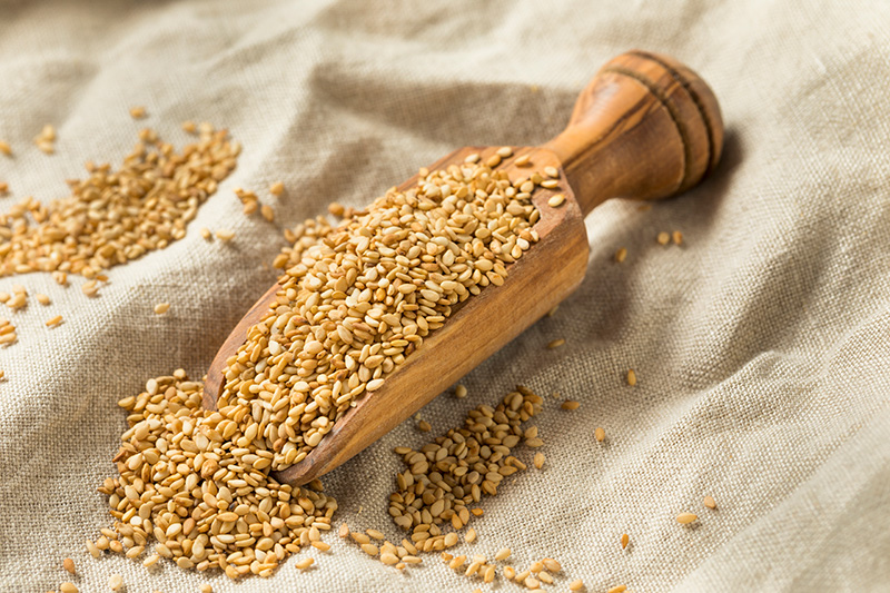 Toasted sesame seeds spilling from a wooden scoop