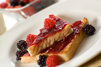 a plate of toast spread with jam along with fresh raspberries and blackberries