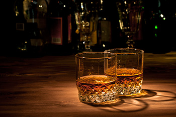 two old-fashioned glasses full of whiskey against a club-like background