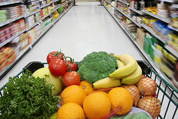 a grocery cart full of fruits and vegetables from the perspective of one pushing the cart