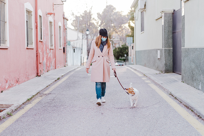 a woman wearing a mask walking a small dog