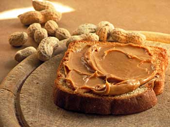a slice of bread spread with peanut butter flanked by several peanuts in the shell