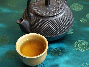 a cup of green tea and an iron teapot