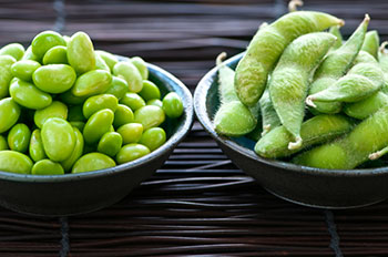 a bowl of edamame in the shell and a bowl of shelled edamame