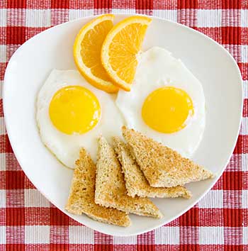 a breakfast meal of fried eggs and toast garnished with slices of orange
