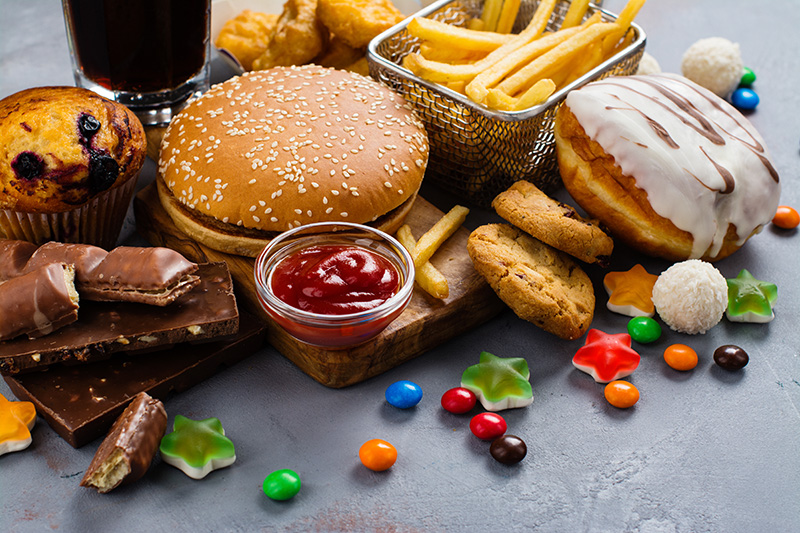 junk food, including a fast food burger, fries, sugary cola, pastries made with refined flours and sugar, candies, and chocolate