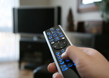 a hand holding a television remote with a television in the background