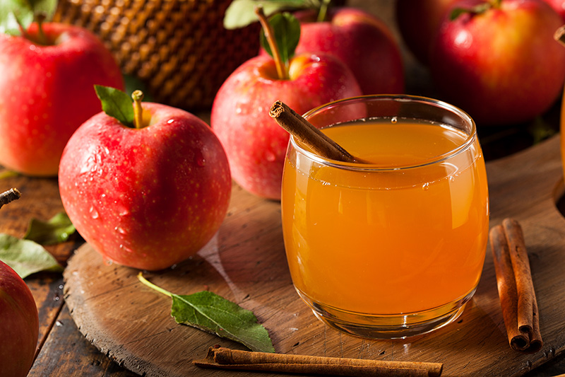 fresh apples and a glass of apple cider garnished with a cinnamon stick