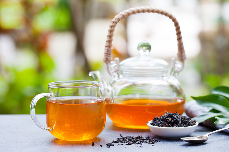 a clear glass teapot full of black tea and a glass teacup full of tea
