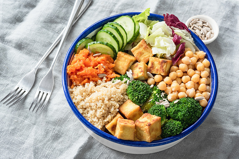 a vegan dish containing quinoa, broccoli, tofu, cucumber, and chickpease
