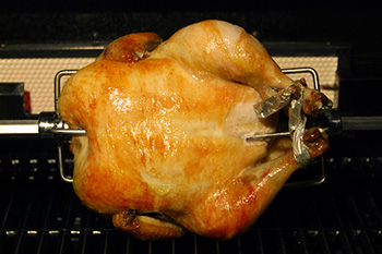 a whole chicken cooking on a rotisserie