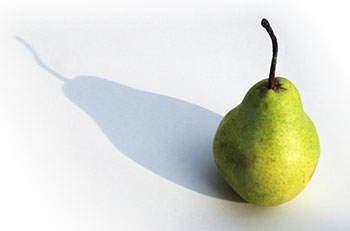 a green pear casting a shadow on a plain white table