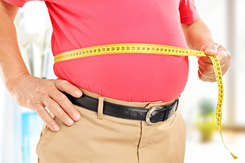 an overweight person measuring their waist with a tape measure